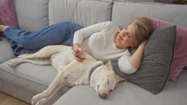 Genç bir kadın akıllı telefon kullanırken köpeği ile koltukta dinleniyor..