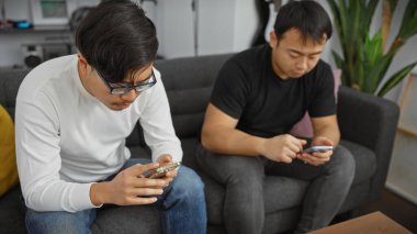 İki adam bir kanepede akıllı telefon kullanıyor, modern bir oturma odasında gündelik, bağlı bir yaşam tarzı sürdürüyorlar..