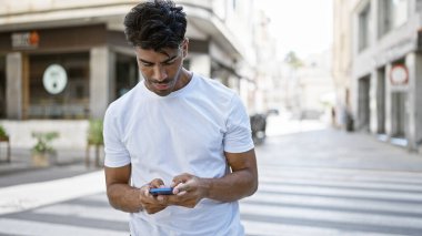 Yakışıklı İspanyol adam şehir caddesinde akıllı telefon kullanıyor. Şehirli, sıradan, bağlantılı, net bir odak noktası olan yaşam tarzı kavramları..