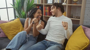 A happy couple with a television remote joyfully celebrating in their cozy living room. clipart