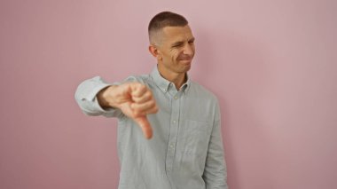 Genç bir adam pembe bir arka plana karşı izole edilmiş bir şekilde baş parmak işareti veriyor, sıradan bir ifade ve jestle onaylamıyor..