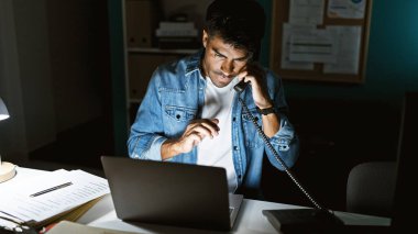Geceleri loş bir ofiste dizüstü bilgisayarla konuşan yakışıklı İspanyol bir adam..