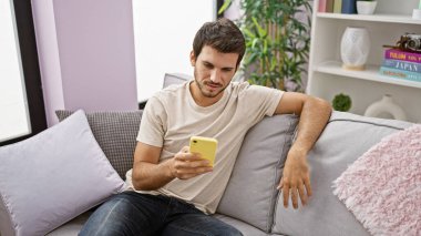 İspanyol adam akıllı telefon kullanıyor modern oturma odasındaki kanepede uzanıyor.
