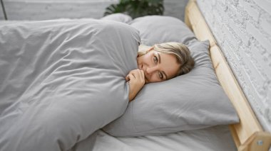 Güzel sarışın kadın huzurlu bir yüz ifadesiyle yatakta uzanıyor, rahat bir yatak odası ortamında, rahatlama ve rahatlama portresi çiziyor..
