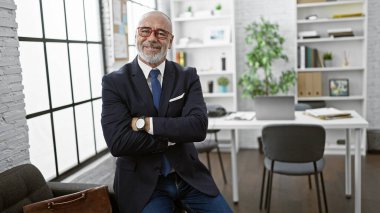 Kendine güvenen, sakallı ve gözlüklü bir iş adamı modern ofis ortamında gülümser.