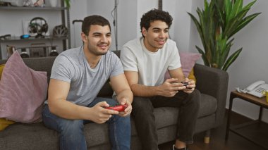 İki genç adam, rahat bir oturma odasında oynuyorlar, birlikte vakit geçiriyorlar..