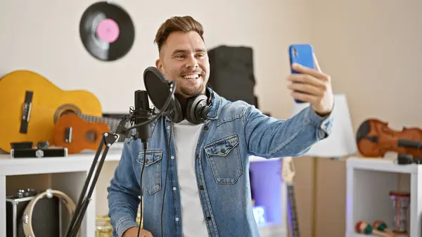 stock image Smiling young man taking selfie in music studio surrounded by guitar and recording equipment