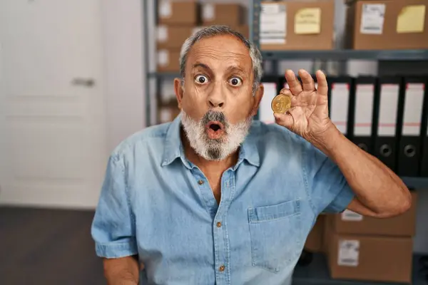 stock image Shock and awe! senior man with white hair astonished by bitcoin coin in office, open-mouthed with disbelief and amazed expression