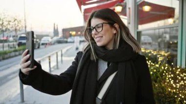 İstanbul caddesinde akıllı telefon kullanan gülümseyen kadın, şehir geçmişini aydınlatan akşam ışıkları.