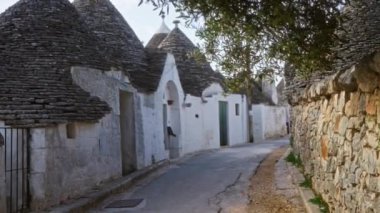 İtalya, Alberobello 'da pitoresk bir sokak. Konik çatıları ve Akdeniz güneşinin yumuşak ışığı altında taş duvarları olan ikonik trullo evler sergiliyor..