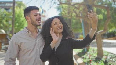 Gülümseyen adam ve kadın güneşli parkta selfie çekiyorlar.
