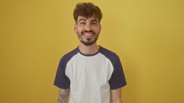 Heyecanlı genç İspanyol bir adam, başarıyı kutluyor, kollarını izole edilmiş sarı arka plana kaldırmış, neşeli bir 'evet' ilan ediyor! Kazanarak.