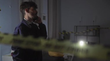 İspanyol dedektif telefonda, kapalı mekan suç mahallinde. Dikkat bandı ve karanlık bir ortam var.