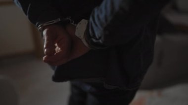 Karanlık bir suç mahallinde elleri kelepçeli bir adam, kanıt ve kanlı çarşaflarla, kapalı bir mekanda şiddet eylemi olduğunu gösteriyor..