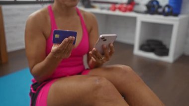 Elinde telefon ve kredi kartı olan bir kadın spor salonunda pembe giyen yetişkin bir kadın.