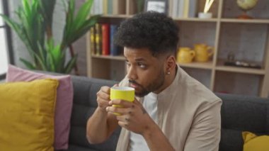 Rahat bir adam, kitaplarla ve renkli yastıklarla dolu rahat bir oturma odasında kahvenin tadını çıkarır..