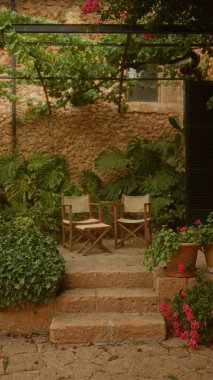 Taş basamaklı veranda, yemyeşil bitkiler, iki sandalye ve bir pergola altında canlı çiçekler sakin bir açık hava inzivası oluşturur.
