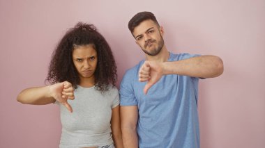 A man and woman stand against a pink background, both showing thumbs down with discontent expressions. clipart