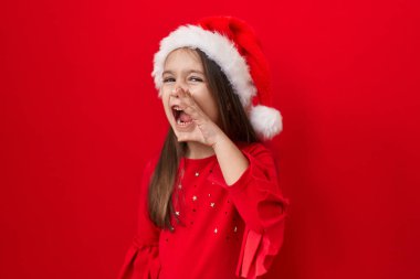 Tapılası İspanyol kız Noel kararından bihaber, yılbaşı şapkası takıyor, jesti yok. Kırmızı izole arkaplanda karışık duygu.