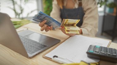 Bir ofiste dizüstü bilgisayar ve hesap makinesiyle Macar forintini analiz eden genç bir kadın..