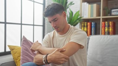 Yakışıklı İspanyol bir adam, kanepede otururken dirsek ağrısı çekiyor.