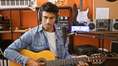 Bir kayıt stüdyosunda mikrofonla gitar çalan İspanyol bir adam.