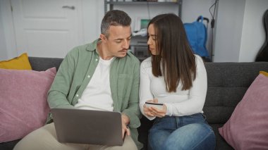Bir adam ve bir kadın yakın bir koltukta oturuyor. Laptop ve kredi kartıyla kapalı bir yerde..