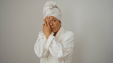 Beyaz bornoz ve havlu giymiş bir kadın. Yüzü el ele kapanıyor. İzole edilmiş beyaz bir arkaplanı var..