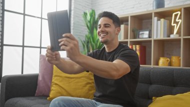 Gülümseyen İspanyol adam modern bir apartman dairesinde selfie çekiyor.