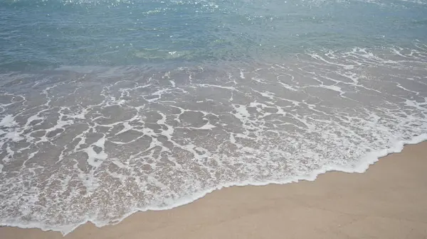 stock image A tranquil beach scene depicting gentle waves lapping against a sandy shore under a clear sky.