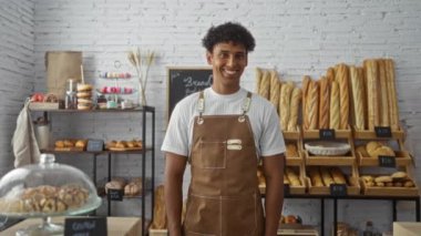 Genç, İspanyol asıllı, gülümseyen ve el kol hareketi yapan bir fırında çeşitli ekmek ve hamur işleri sergileniyor.