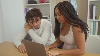 Modern bir oturma odasında dizüstü bilgisayarla tartışan bir erkek ve kadın, rahat bir ev ortamını yansıtıyor..