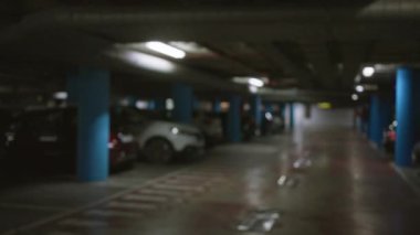 Arka planda loş ışıklandırmanın altında mavi sütunları ve arabaları olan boş bir yeraltı otoparkının odaklanmış görüntüsü.