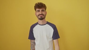 Genç, başarılı İspanyol bir adam izole edilmiş sarı bir arka planda duruyor, gülümsüyor ve elleriyle iyi bir işaret veriyor, pozitifliğini ve güvenini ifade ediyor.