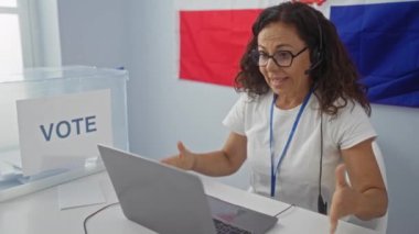 Dominik Cumhuriyeti 'nde seçmen odasında konuşan bir kadın. Video görüşmesi sırasında. Arka planda oy işareti ve bayrak var.