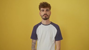 Işıl ışıl gülümseyen genç İspanyol adam, izole edilmiş sarı bir arka plana karşı neşeli bir şekilde duruyor, şakayla kamerayı işaret ediyor, mutlu titreşimler yayıyor ve iyi bir mizah yayıyor.