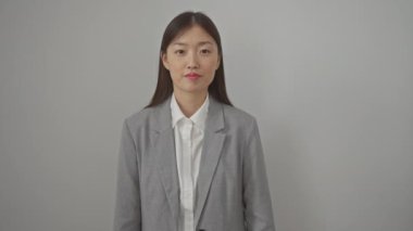 Genç, pozitif ve gülümseyen Çinli kadın çapraz kollarıyla rahat duruyor, beyaz izole edilmiş arka planda şık bir ceket giyiyor, kendinden emin ve mutlu görünüyor.