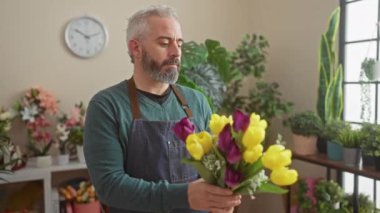 Yeşil bitkiler ve çiçeklerle dolu bir çiçekçide elinde renkli laleler tutan yakışıklı sakallı adam..