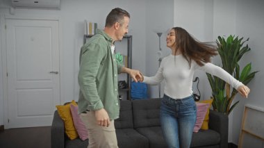 Neşeli bir erkek ve kadın, iyi ışıklandırılmış bir apartman dairesinde, mutlu ilişkilerini ifade ederek dans ediyorlar..