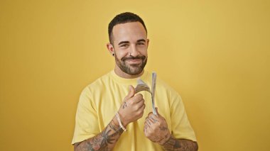 Sarı arka planda para tutan mutlu dövmeli bir adam.