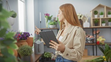 Genç bir kadın, bitkilerle dolu bir iç odada tabletle etkileşime giriyor. Bu, doğanın ortasındaki teknolojinin bir örneği..