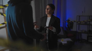 Bir kadın müfettiş, şüpheli bir adamı polis bandıyla işaretlenmiş loş bir evin içinde sorguluyor..