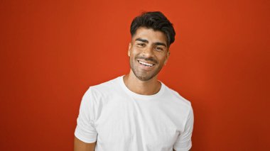 Yakışıklı, genç, İspanyol bir adam canlı, kırmızı, izole bir arka plana gülümsüyor.