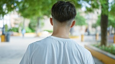 Keyifli bir şehir parkında güneşli bir günün tadını çıkaran sıradan tişörtlü genç bir adamın arka görüntüsü..