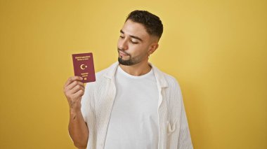 Sarı duvarda Türk pasaportu inceleyen yakışıklı adam.