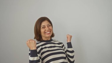 Çizgili tişörtlü, neşeli, orta yaşlı İspanyol bir kadın beyaz bir arka plana karşı neşeli bir ifadeyle kutlama yapıyor..