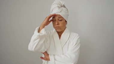 Kafasına havlu ve bornoz geçirmiş bir kadın, beyaz arka planda soyutlanmış, orta yaşlı ve stresli, sorun, kriz ve endişeye kapılmış.