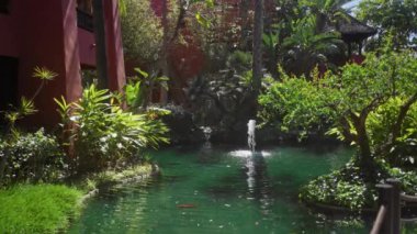 Bereketli bir yeşillik, dingin bir gölet ve geleneksel bir çardak içeren sakin bir tropikal bahçe..