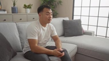 Yakışıklı Asyalı genç adam heyecanlı bir şekilde evinde televizyon izliyor..