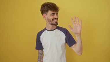 Kendinden emin genç İspanyol adam mutlu bir şekilde gülümsüyor, parmaklarıyla beş numarayı gösteriyor, izole edilmiş sarı arka planda dikiliyor ve işaret ediyor.
